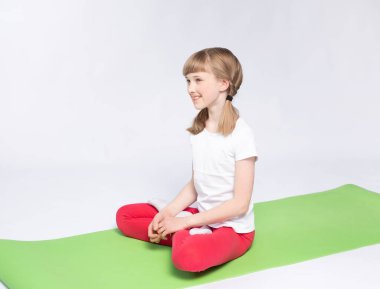 Genç kız yerde egzersiz yapıyor, paspasın üzerinde oturuyor.