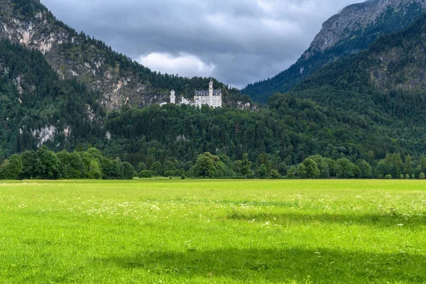 Royal castle in the mountains on the background of storm clouds and sunlit meadow in the foreground