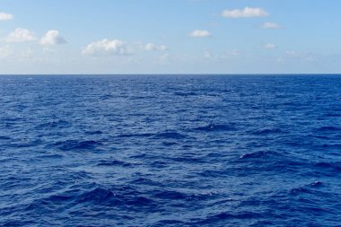 Okyanusun masmavi suları üzerinde beyaz bulutlarla mavi gökyüzü.