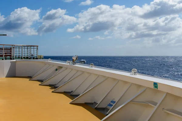 Mavi denize karşı çitleri olan sarı güverte ve ufukta bulutlu gökyüzü..