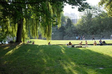 Münih, Almanya - Ağustos 2018: Vatandaşlar gölgeli bir şehir parkında kavurucu güneşin içinde rahatlıyor.