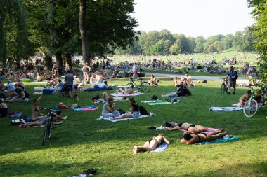 Münih, Almanya - Ağustos 2018: Vatandaşlar gölgeli bir şehir parkında kavurucu güneşin içinde rahatlıyor.