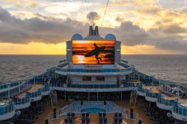 Karayipler, Atlantik Okyanusu - Ocak 2018: Gün batımı gökyüzünün arka planında, gün batımı arka planında sörf tahtası olan bir adam figürüne sahip büyük bir Tv ekranı yla yolcu gemisi Royal Princess'in üst güvertesi