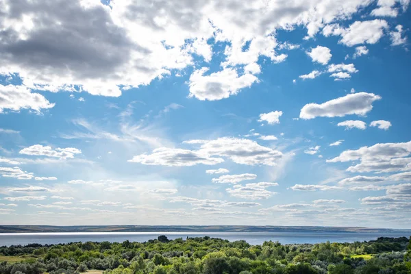Ormanlık kıyılarda güneş parlaması ve mavi gökyüzünde bulutlar ile geniş, tam akan nehir görünümü. Volga nehri.