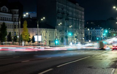 Uzun pozlama, ıslak asfalt üzerinde bir gece şehrinin arka planında hafif ulaşım izleri..