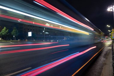 Uzun pozlama, ıslak asfalt üzerinde bir gece şehrinin arka planında hafif ulaşım izleri..