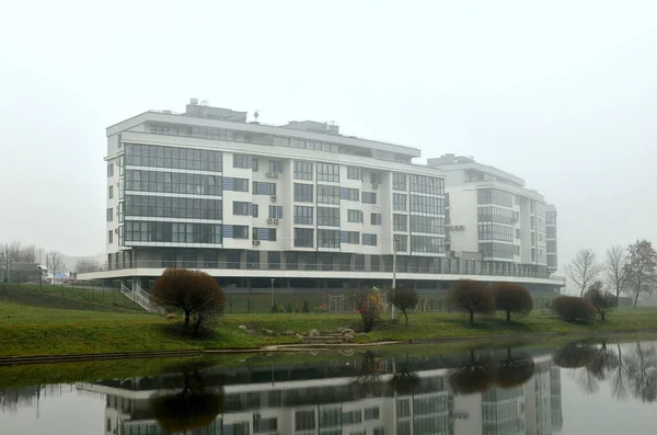 Designer residential apartment building on the background of the autumn river landscape. Heavy fog in the city