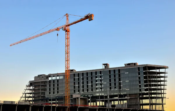 Industrial construction cranes and building silhouettes over sun at sunrise. Abstract Industrial background  of blue sky and clouds