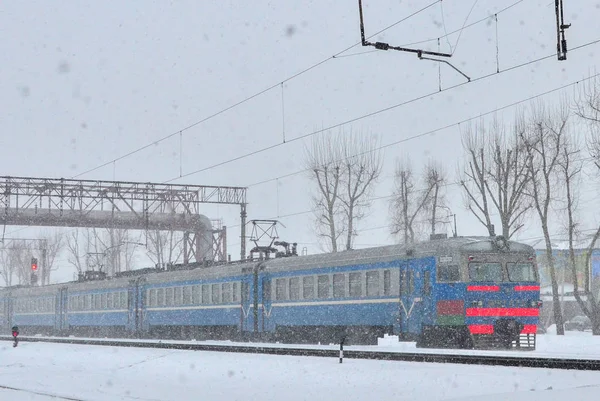 Passenger train on the railway moves in a large snow blizzard in winter
