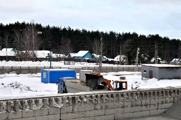 View from the top to work in a career with bulk cargo. A bulldozer with a bucket loads crushed stone into a dump truck with a body near a high unloading railway platform.