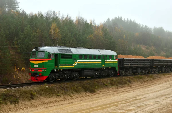 Freight train transports sand with freight wagons in a sand pit in cloudy foggy weather. Logistics of cargo delivery by rail