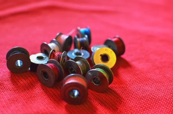 Small metal reels with colored cotton threads for sewing machines on a red wool background