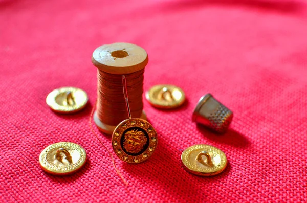 Accessories for sewing and darning clothes: needle, thread and thimble on a red background of wool fabric. Gold designer buttons with crystals or diamonds swarovski