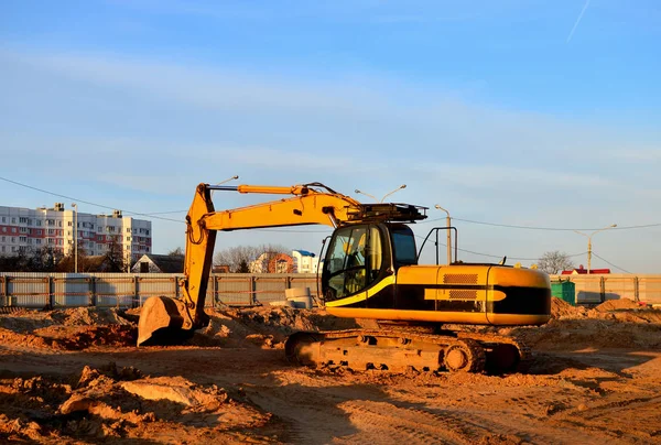 Tracked excavator with a bucket in the ground at a construction site against a blue sky and sunset