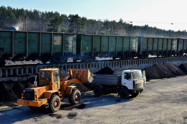 Wheel loader excavator loads coal into a dump truck at a cargo railway station