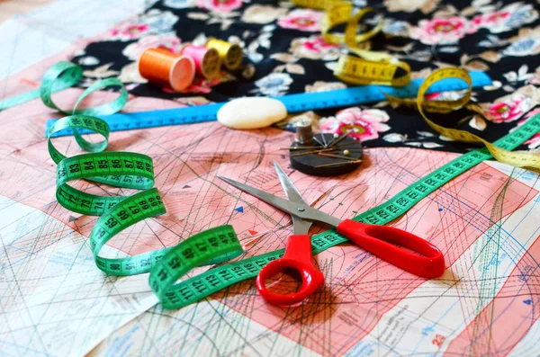 Essentials of the measuring and cutting textile or fine cloth. Work table of a tailor: Ruler, pattern, scissors, thread, needle, cloth, drawing tool, thimble. Tailoring industry dressmaking tools