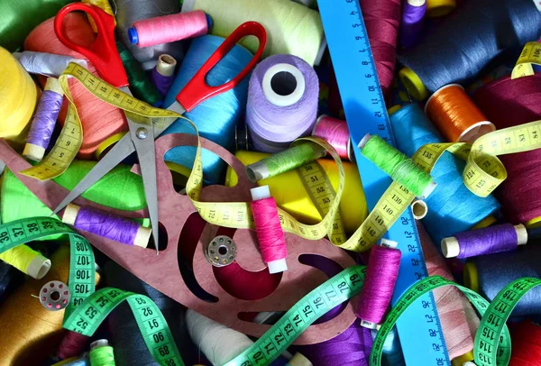 Background of bobbins with multicolored threads for sewing. Needlework, sewing and tailoring concept. Essentials of the measuring and cutting textile or fine cloth. Tools of a tailor, ruler, scissors.