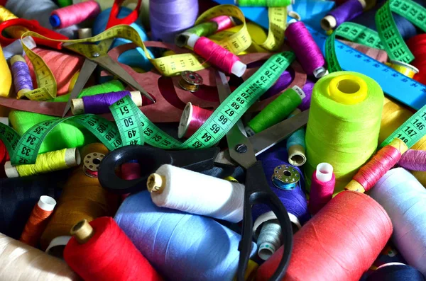 Background of bobbins with multicolored threads for sewing. Needlework, sewing and tailoring concept. Essentials of the measuring and cutting textile or fine cloth. Tools of a tailor, ruler, scissors.