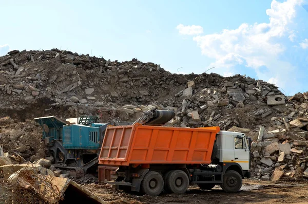 Excavator loads construction waste into reinforced concrete mobile shredder for crushing, recycling of construction mixed waste. Broken concrete recycling at industrial landfill. Screening plant