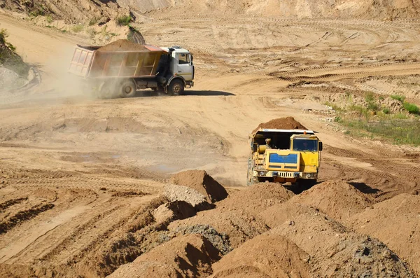 Big yellow dump trucks working in the open-pit. Transporting sand and minerals. Mining quarry for the production of crushed stone, sand and gravel for use in the construction industry - image