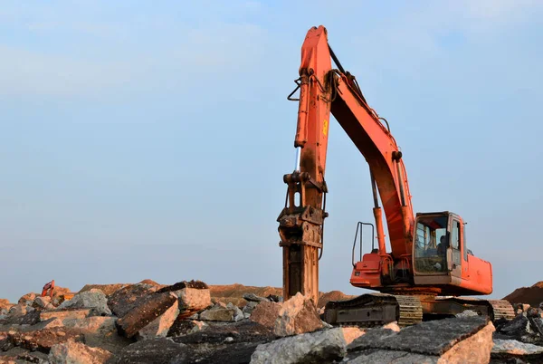 Crawler excavator with hydraulic hammer for the destruction of concrete and hard rock at the construction site. Salvaging and recycling building and construction materials, concrete demolition waste