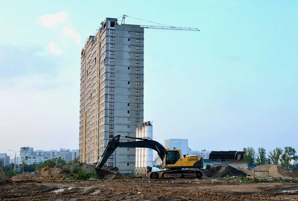 The excavators on the construction site against the background of a high multi-storey residential complex and tower cranes. Excavation, digging trenches for sewer pipes and utilities