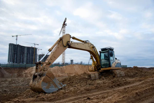 Excavator at earthworks on construction site. Backhoe loader digs a pit for the construction of the foundation. Digging trench for laying sewer pipes drainage in ground. Earth-Moving Heavy Equipment