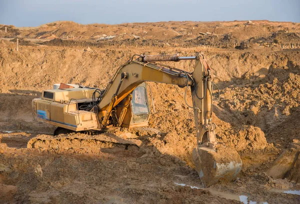 Excavator at earthworks on construction site. Backhoe loader digs a pit for the construction of the foundation. Digging trench for laying sewer pipes drainage in ground. Earth-Moving Heavy Equipment