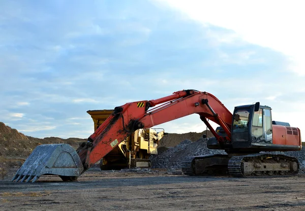 Excavator with a large iron bucket breaks asphalt on a construction site. Demolition work concrete, replacing asphalt, road works. Mobile Stone crusher machine at backhoe crawler