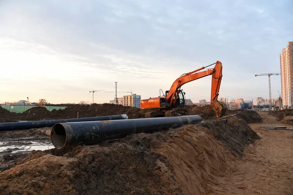 Red excavator during groundwork on construction site. Hydraulic backhoe on earthworks. Heavy equipment for demolition, construction and ground works. Digging foundation and laying storm sewer pipes