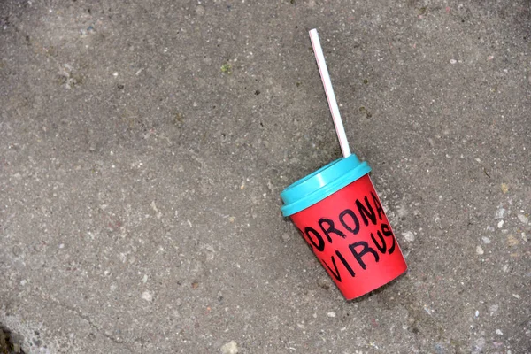 COVID-19-Ausbruch: Rote Kaffeetasse aus Papier mit der Aufschrift CORONAVIRUS liegt auf dem Bürgersteig einer leeren Straße am Virengrund Null. — Stockbild Covid Ausbruch Rote Kaffeetasse Aus Papier Mit Der Aufschrift Coronavirus — Stockfoto