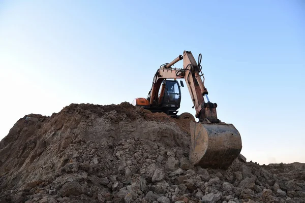Bucked wheel excavator on earthmoving. Backhoe digs ground in sand quarry on blue sky background. Construction machinery for excavation, loading, lifting and hauling of cargo on job sites
