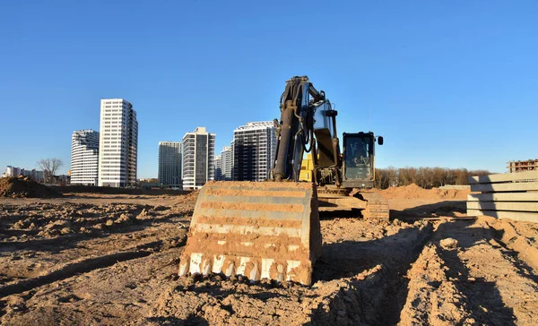 Excavators at earthworks on construction site. Backhoe loader digs a pit for the construction of the road. Digging trench for laying sewer pipes drainage in ground. Earth-Moving Heavy Equipment