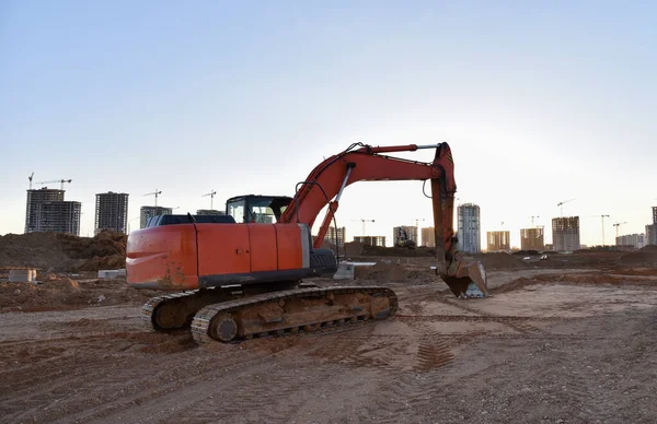 Excavator working at construction site on earthworks. Backhoe on road work digs ground. Paving out sewer line. Construction machinery for excavating, loading, lifting and hauling of cargo