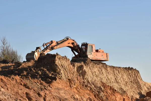 Excavator during earthmoving at open pit on blue sky background. Construction machinery and earth-moving heavy equipment for excavation, loading, lifting and hauling of cargo on job sites