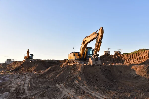 Excavators working at construction site on earthworks. Backhoe digging building foundation. Paving out sewer line. Construction machinery for excavating, loading, lifting and hauling of cargo
