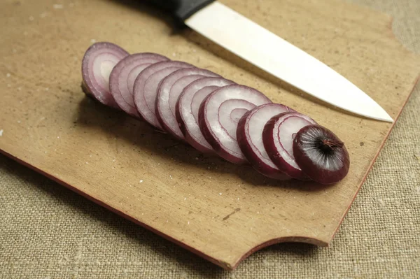 red onion sliced rings on a wooden board. white ceramic kitchen knife