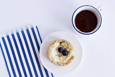 Yaban mersini, çay bardağı ve masada mavi çizgili kağıt torba ile pasta