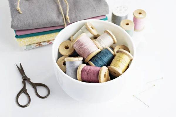Vintage thread spools in white cup, retro scissors and cotton fabrics
