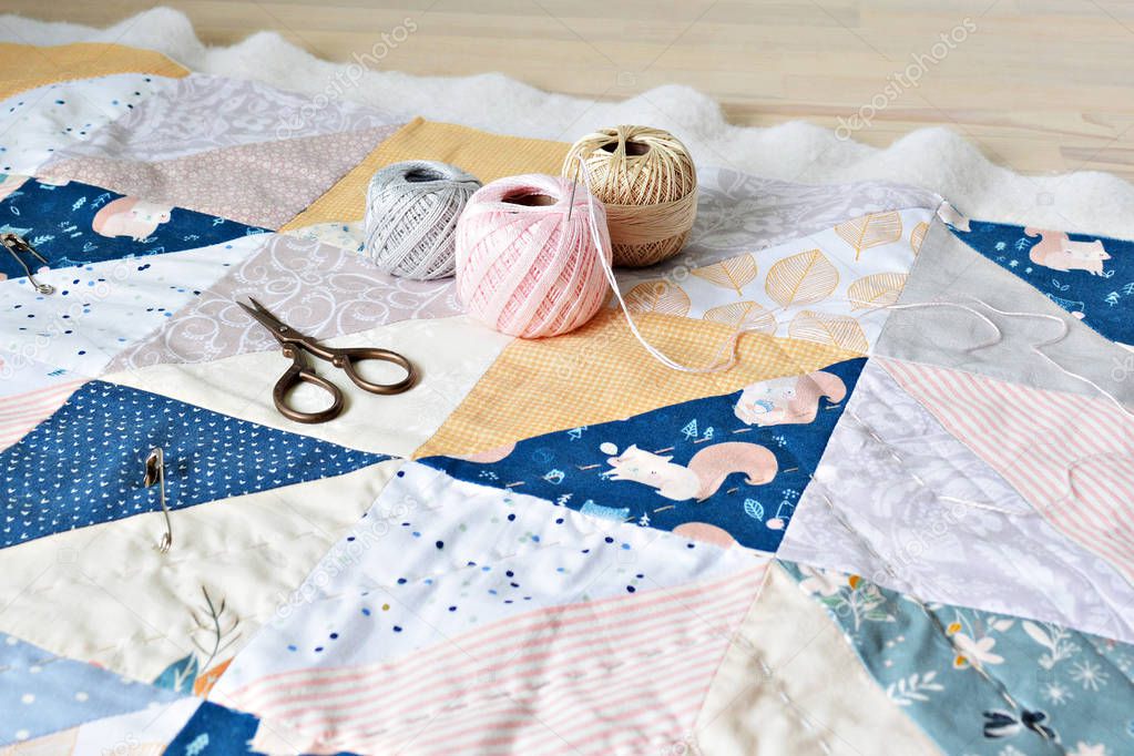 Hand stitch quilting process: cotton thread, needle and scissors on the table