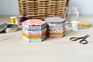 Ahşap masa üzerinde Altıgen patchwork şablonları, iplik, retro makas, metal iğneler, cam kavanoz ve rattan sepet