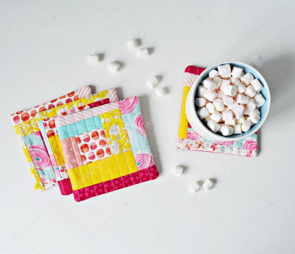 Set of quilted patchwork colorful coasters and white cup with marshmallows