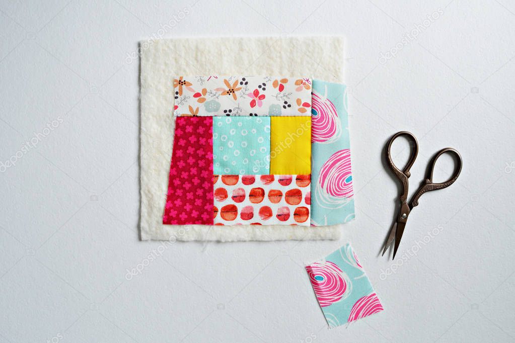 Colorful fabric scraps, batting and scissors over white