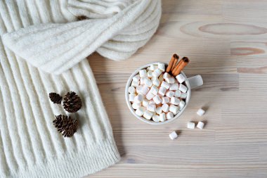 Beyaz yün kazak, çam eksilerini ve ahşap masada marshmallow ve tarçın ile fincan