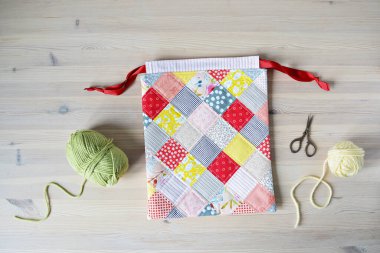 Renkli yama iplik torbası, yeşil ve sarı iplik, ahşap masada makas. 