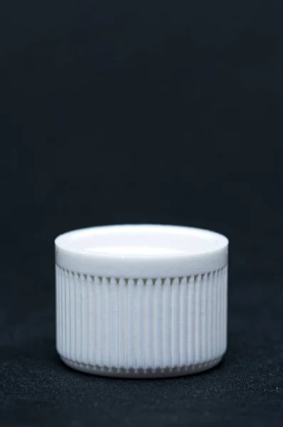 Plastic white cap on black background. Manufactured object
