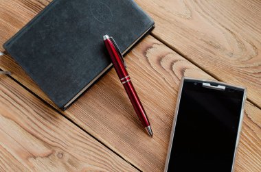 Kolu, telefon ve ahşap bir masa üstünde defter