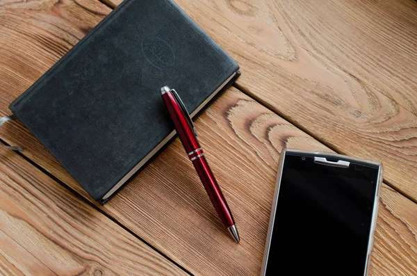 Kolu, telefon ve ahşap bir masa üstünde defter