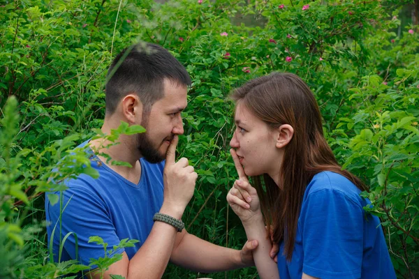 A pair of young people in nature sit in the bushes.