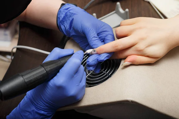 The master of nail service aligns the nails to the client with an electric machine.